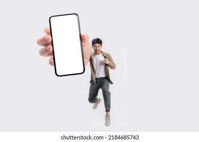 Full length of cheerfull Asian man jumping and smiling in air with showing cellphone blank screen with empty space for mobile app on screen. Isolated in studio white background. Creative collage. - Powered by Shutterstock