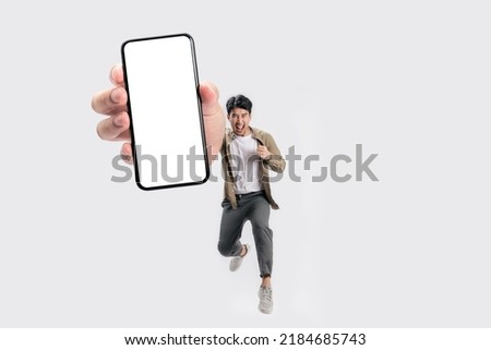Full length of cheerfull Asian man jumping and smiling in air with showing cellphone blank screen with empty space for mobile app on screen. Isolated in studio white background. Creative collage.