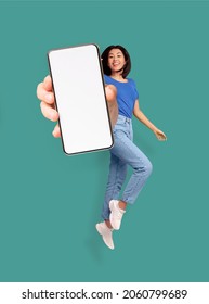 Full length of cheery Asian woman jumping and smiling, showing cellphone with empty space for mobile app or website on screen, turquoise studio background, mockup. Creative collage - Shutterstock ID 2060799689