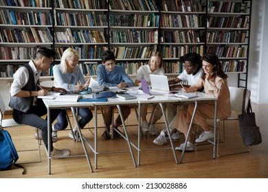Full length concentrated team of multiethnic millennial college university students studying sitting together at big table, working on project in library using gadgets and paper books, writing notes. - Shutterstock ID 2130028886