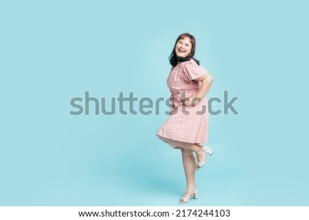 Full length Confidence cheerful beautiful smile Asian woman plus size in pink pastel dress on isolate light blue studio background. Fashion young female chubby confident concept.