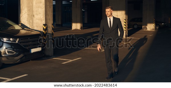 Full length of confident mature man in full suit\
walking by parking lot