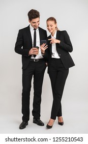 Full length of confident young business couple standing isolated over gray background, holding cups of takeaway coffee, using mobile phone