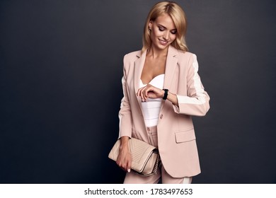 Full length of confident young woman in smart casual wear checking the time while standing against grey background. - Powered by Shutterstock