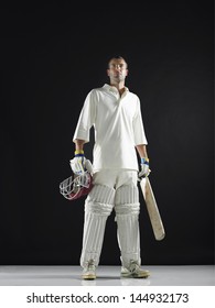 Full Length Of A Cricket Player Holding Bat And Helmet Against Black Background