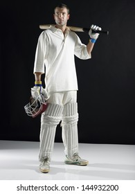 Full Length Of A Cricket Player Holding Bat On Shoulder Against Black Background