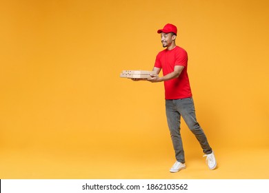 Full length delivery employee african man 20s in red cap blank print t-shirt uniform work courier dealer service concept hold give food order pizza cardboard boxes isolated on yellow background studio