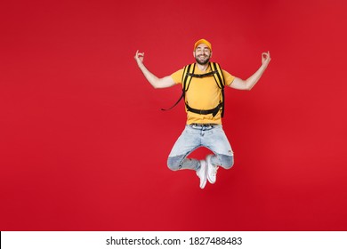 Full Length Delivery Employee Man Male In Yellow Cap T-shirt Uniform Thermal Food Bag Backpack Work Courier Service During Quarantine Covid-19 Virus Jumping Yoga Isolated On Red Background Studio