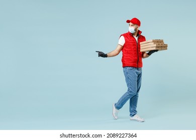 Full Length Delivery Guy Employee Man In Red Cap T-shirt Vest Uniform Face Mask Work Courier Service Covid-19 Flu Virus Hold Pizza In Cardboard Flatbox Run Go Walk Isolated On Pastel Blue Background