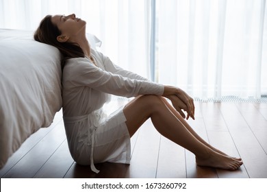 Full Length Desperate Depressed Young Brunette Woman Sitting On Floor, Leaning Back On Bed, Regretting Wrong Decision, Thinking Of Troubles, Relations Problems Break Up Divorce Alone In Bedroom.