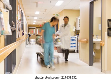 Full length of doctor and nurse pulling stretcher in hospital corridor