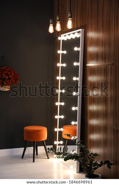 Full length dressing mirror with lamps and stool\
in stylish room interior