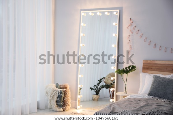 Full length dressing mirror with lamps in\
stylish bedroom interior