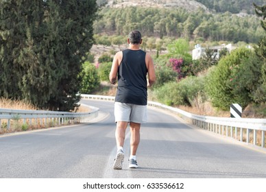 Full Length Elderly Man In Gray Shorts And Black Shirt Sportswear Running On Road Near The Nature-blossom Tree And Flowers.Back View.Close-up.Jog Workout,healthy Lifestyle,well-being .Soft Focus.