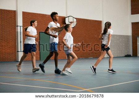 Full length of elementary students running while having PE class at school gym.