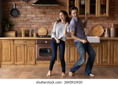 Full Length Emotional Cheerful Laughing Young Hispanic Family Couple Dancing Barefoot On Warm Heated Wooden Floor In Stylish Kitchen, Listening Energetic Disco Music, Having Fun Together In Own House.