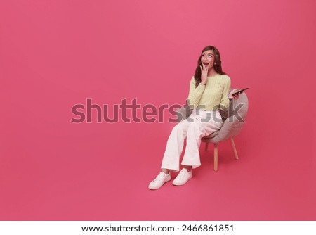 Full length excited beautiful Asian teen woman using smartphone and sitting on chair isolated on pink copy space background. People lifestyle Technology Concept.