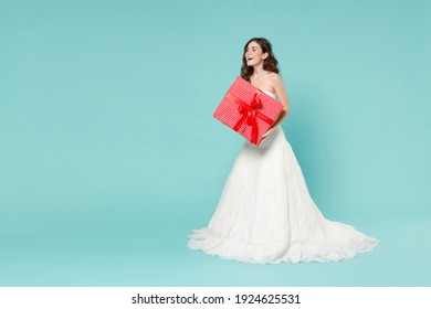 Full length excited bride young woman in white wedding dress hold red present box with gift ribbon bow looking aside isolated on blue turquoise background studio. Ceremony celebration party concept - Powered by Shutterstock