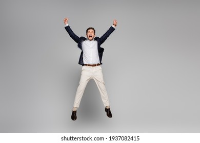 full length of excited man with outstretched hands jumping on grey - Shutterstock ID 1937082415