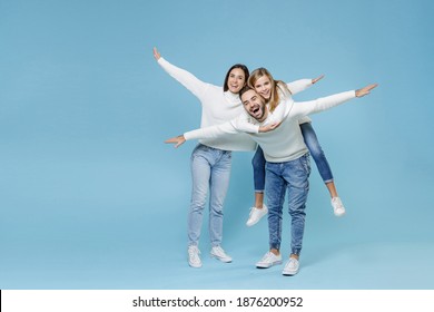 Full Length Of Excited Young Parents Mom Dad With Child Kid Daughter Teen Girl In Sweaters Giving Piggyback Ride To Joyful, Sitting On Back Isolated On Blue Background. Family Day Parenthood Concept