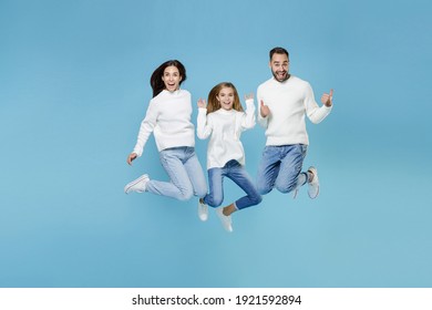 Full length of excited young parents mom dad with child kid daughter teen girl in white sweaters jumping showing thumbs up isolated on blue background studio portrait. Family day parenthood concept