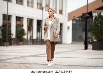 Full length fashionable woman walking Street city and wears trendy business clothes outfit, oversize jacket, tie, pants and white loafer shoes. Confident female model with short blonde haircut - Powered by Shutterstock