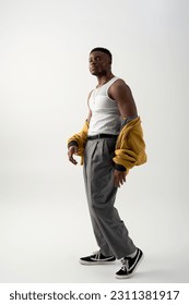 Full length of fashionable young black man in sleeveless t-shirt and bomber jacket standing on grey background, contemporary shoot featuring stylish attire, fashion statement