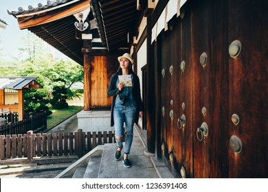 full length of female lens man tourist walking along the wooden door in shitennoji. young lady toursit holding paper map looking around searching the destination of osaka attraction. girl trip in jp.