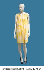 Full length female mannequin wearing yellow dress with flower pattern, isolated on blue background. 