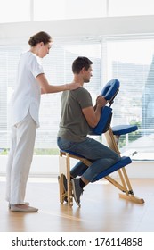 Full Length Of Female Physiotherapist Massaging Man On Massage Chair In Hospital