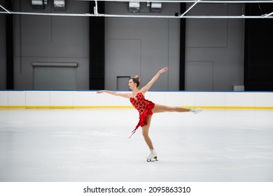 Full Length Of Figure Skater In Red Dress Performing Camel Spin In Professional Ice Arena