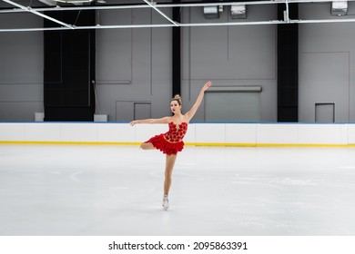 Full Length Of Figure Skater In Red Dress Performing Camel Spin In Ice Arena