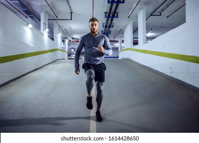 Full length of fit muscular handsome Caucasian sportsman in active wear running in underground garage at night. Urban life concept.