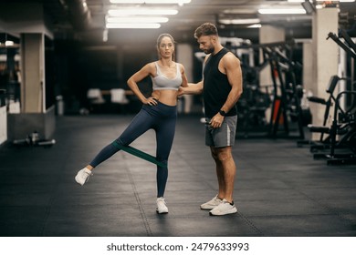 Full length of fit sportswoman in shape doing exercises with resistance band at gym and her trainer is helping her. - Powered by Shutterstock