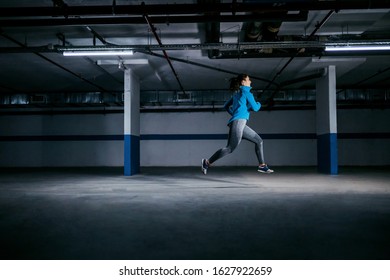 Full length of fit sportswoman in tracksuit running in garage at night. Urban life concept. - Powered by Shutterstock