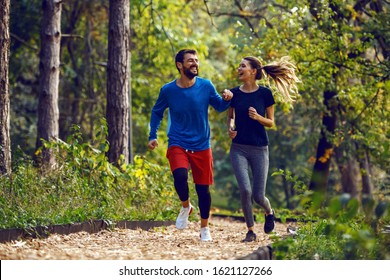 Full Length Of Fit Sporty Happy Caucasian Couple In Sportswear Running In Woods On Trail In Morning.