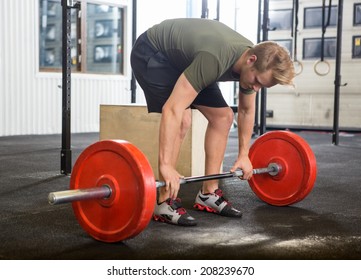 Full length of fit young man picking barbell in box