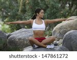 Full length of a fit young woman sitting on stone with arms out in park