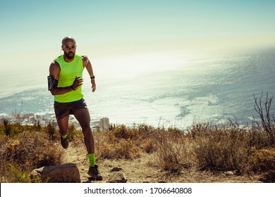 Full length of fitness man running over rocky trail on mountain. Fit young man running up a hill.