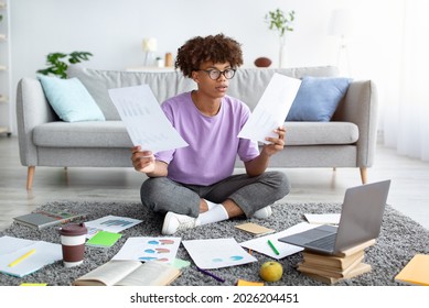 Full Length Of Focused Black Teen Sitting On Floor Among Scattered Documents, Using Laptop To Write Coursework Paper, Studying Remotely, Making College Home Assigment, Indoors