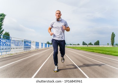 Full length front view on adult caucasian man jogging on the running track - Blonde male athlete in stadium training run in sunny spring or summer day - real people healthy lifestyle concept - Powered by Shutterstock