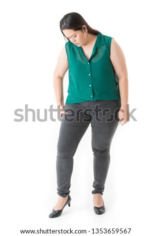 Full length front view of unhappy young, plump, beautiful, Asian lady, in smart casual, green, sleeveless shirt, black pants, black shoes, hand hold excessive fat thigh, on isolated white background