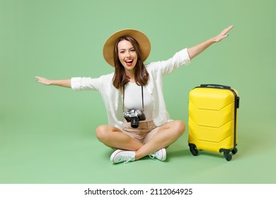 Full length fun happy traveler tourist woman in casual clothes hat suitcase sit with outstretched hands isolated on green background Passenger travel abroad weekend getaway Air flight journey concept