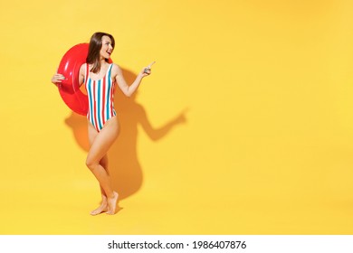 Full length fun happy young sexy woman slim body wear red blue swimsuit pose go with inflatable rubber ring isolated on vivid yellow color background studio. Summer hotel pool sea rest sun tan concept