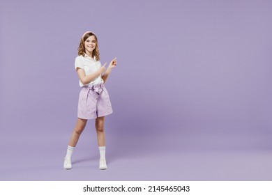 Full length fun little kid girl 12-13 years old in white shirt walk point index finger aside on workspace advert promo area isolated on purple color background. Childhood children lifestyle concept - Shutterstock ID 2145465043