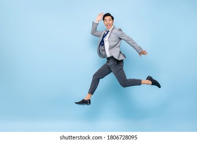 Full length fun portrait of happy energetic young Asian businessman jumping in mid-air isolated on studio blue background with copy space
