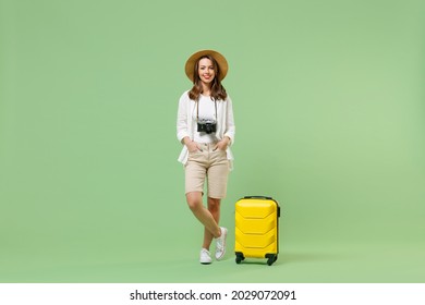 Full length fun traveler tourist woman in casual clothes straw hat hold yellow suitcase isolated on pastel green background. Passenger travel abroad on weekends getaway. Air flight journey concept.