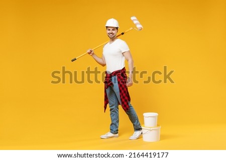 Full length fun young employee handyman man wear t-shirt holding paint roller look camera walk isolated on yellow background Instruments accessories for renovation apartment room. Repair home concept