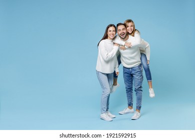 Full Length Of Funny Young Parents Mom Dad With Child Kid Daughter Teen Girl In Sweaters Giving Piggyback Ride To Joyful, Sitting On Back Isolated On Blue Background. Family Day Parenthood Concept