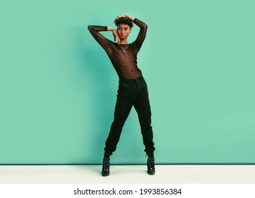 Full length of a gay man in black outfit. Gender fluid man wearing black jeans, black net shirt and high heels posing against blue background.